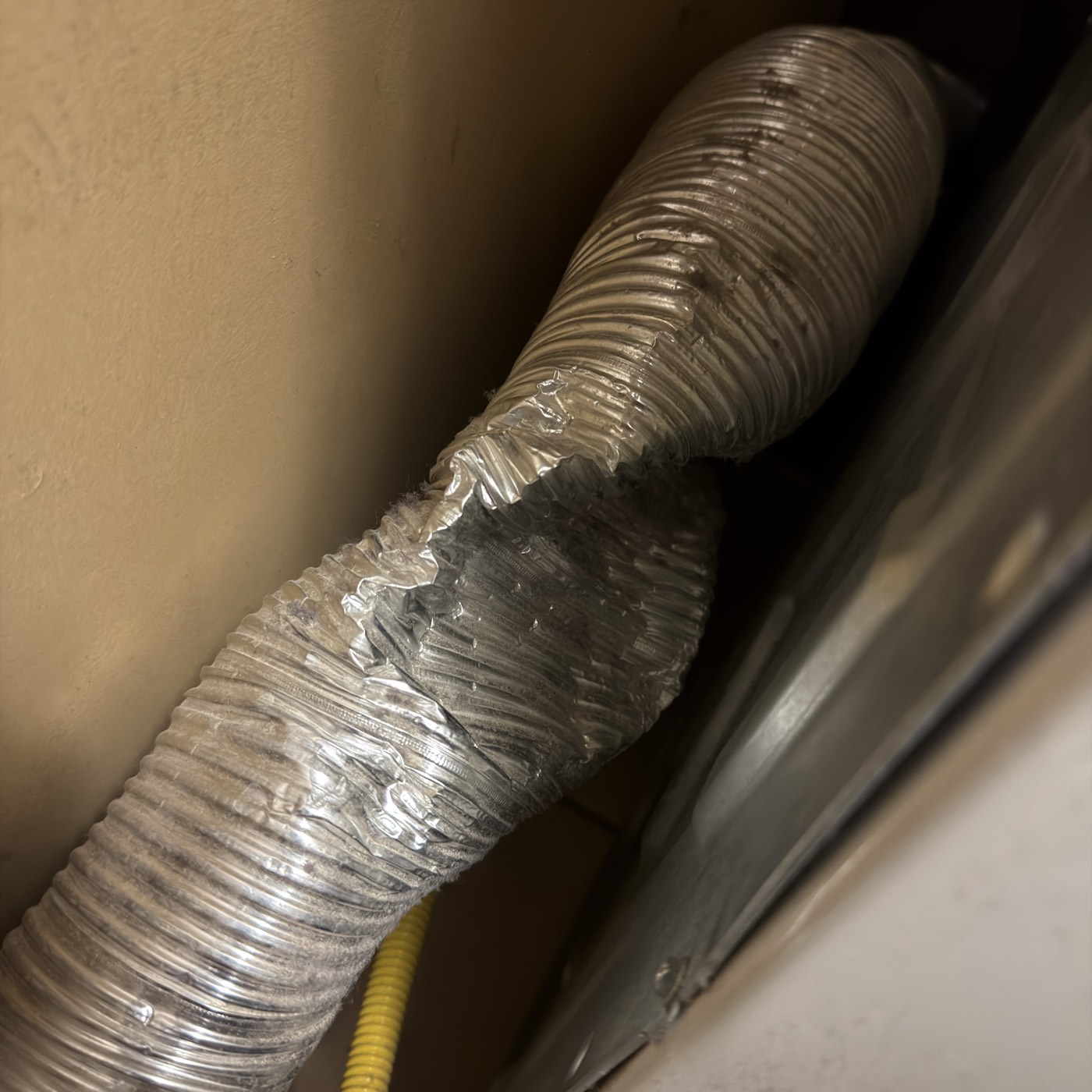 A flexible foil dryer transition hose crushed and kinked flat where it runs behind the machine
